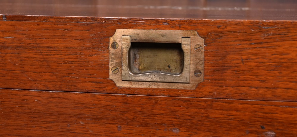 A nineteenth-century rectangular teak coffer with flush brass corner brackets, brass escutcheons, and an inlaid top cartouche, raised on a wooden stand with square legs. View IV