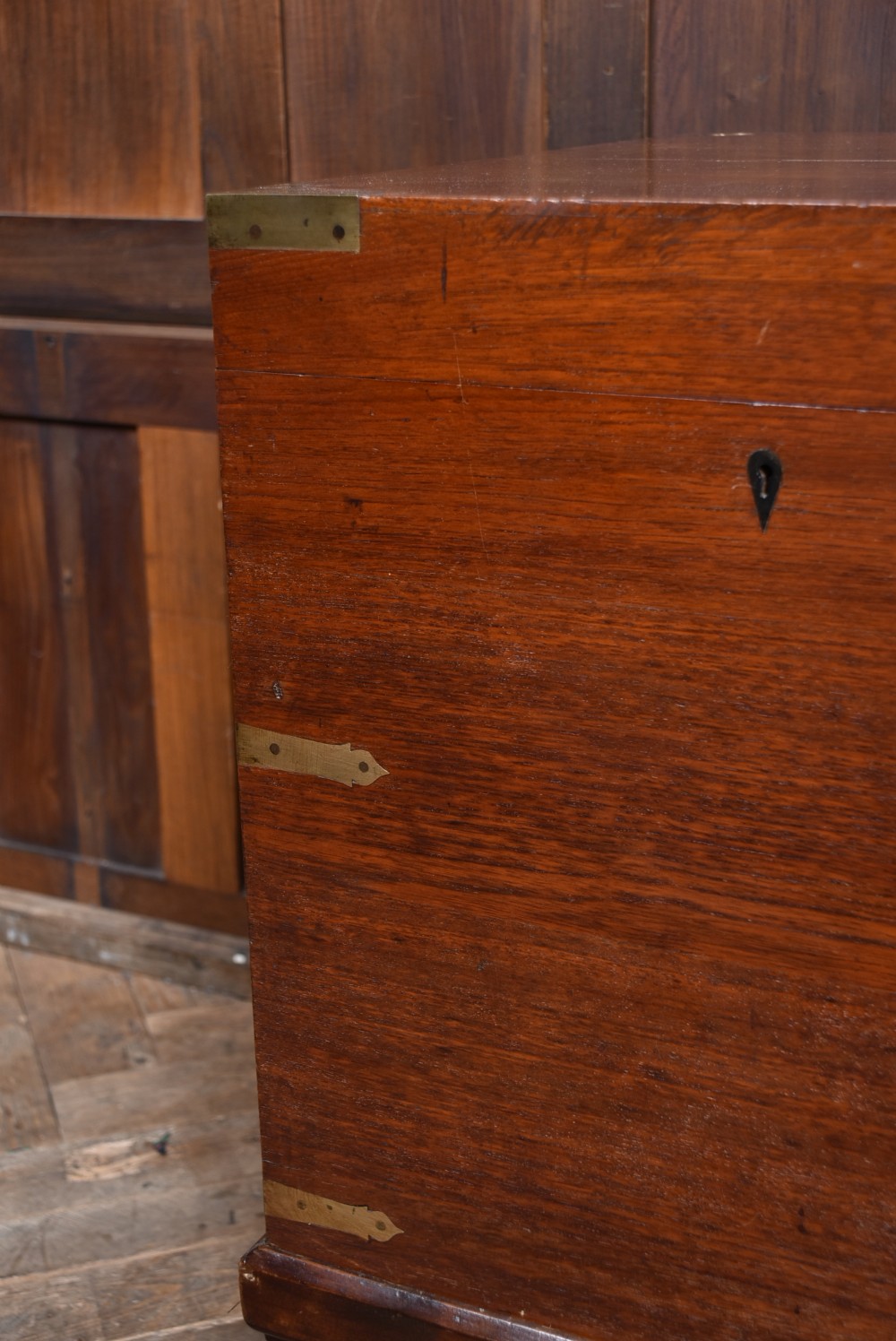A nineteenth-century rectangular teak coffer with flush brass corner brackets, brass escutcheons, and an inlaid top cartouche, raised on a wooden stand with square legs. View V