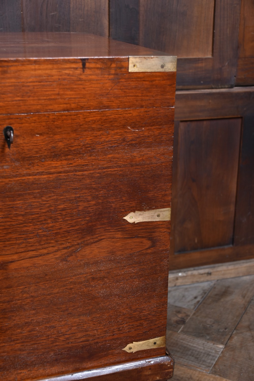 A nineteenth-century rectangular teak coffer with flush brass corner brackets, brass escutcheons, and an inlaid top cartouche, raised on a wooden stand with square legs. View VII