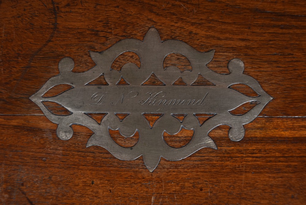 A nineteenth-century rectangular teak coffer with flush brass corner brackets, brass escutcheons, and an inlaid top cartouche, raised on a wooden stand with square legs. View IX