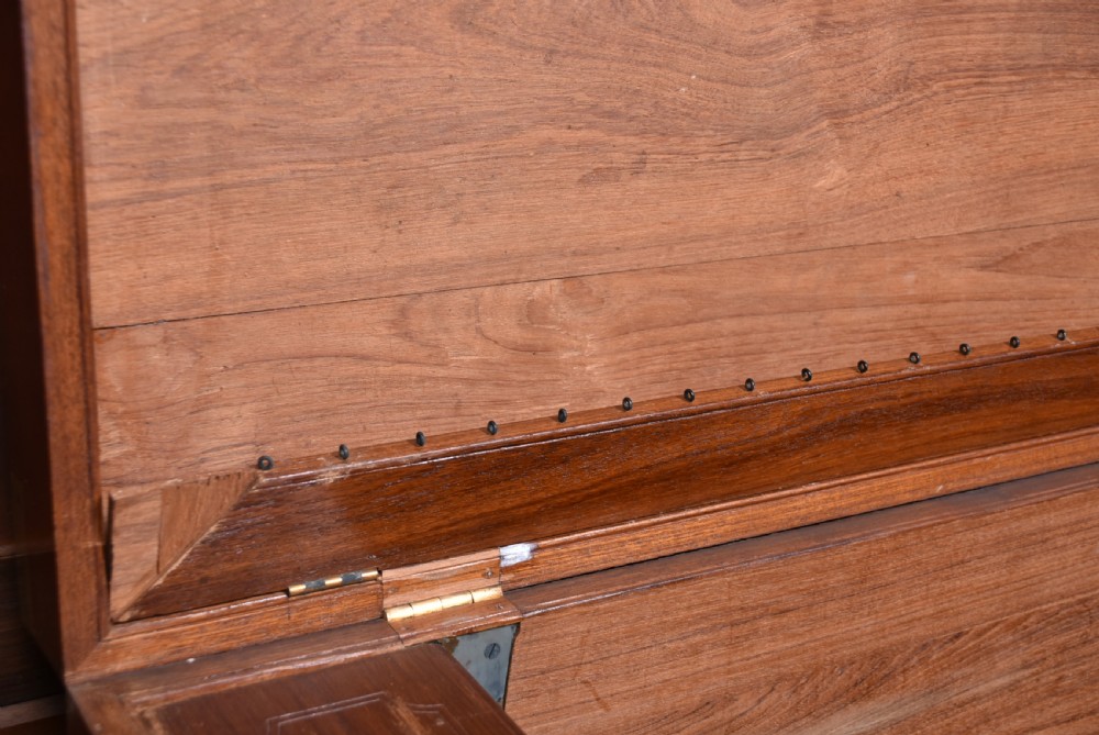 A nineteenth-century rectangular teak coffer with flush brass corner brackets, brass escutcheons, and an inlaid top cartouche, raised on a wooden stand with square legs. View XII