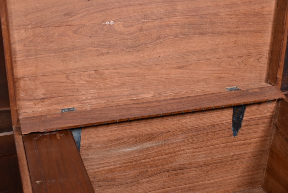A nineteenth-century rectangular teak coffer with flush brass corner brackets, brass escutcheons, and an inlaid top cartouche, raised on a wooden stand with square legs. View XIII