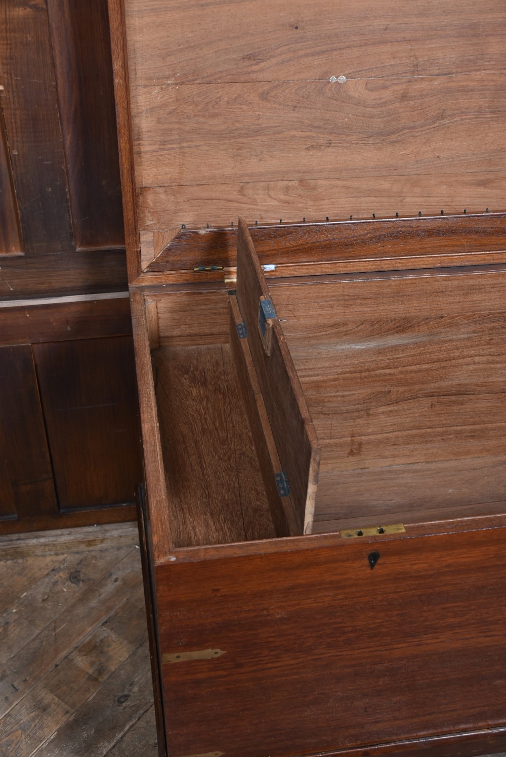 A nineteenth-century rectangular teak coffer with flush brass corner brackets, brass escutcheons, and an inlaid top cartouche, raised on a wooden stand with square legs. View XVI
