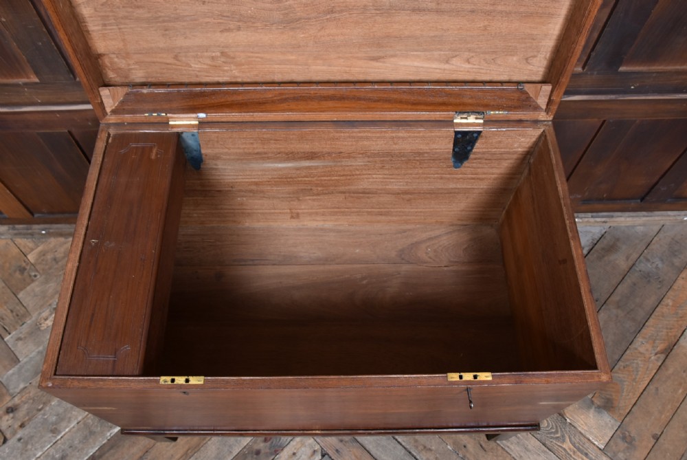 A nineteenth-century rectangular teak coffer with flush brass corner brackets, brass escutcheons, and an inlaid top cartouche, raised on a wooden stand with square legs. View XVIII