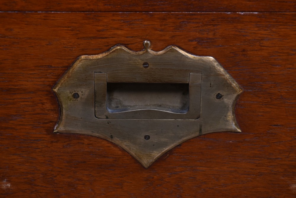 A nineteenth-century rectangular teak coffer with flush brass corner brackets, brass escutcheons, and an inlaid top cartouche, raised on a wooden stand with square legs. View XIX