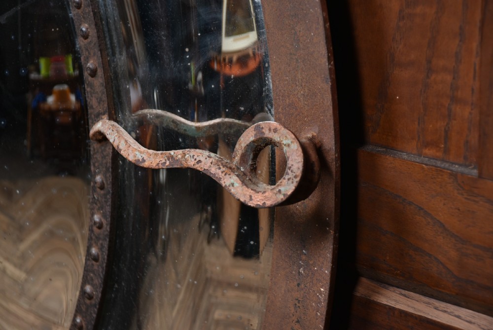 A circular convex wall mirror featuring a patinated dark metal frame, riveted inner rim, forged scroll mounts, and foxed glass reflection. View VIII