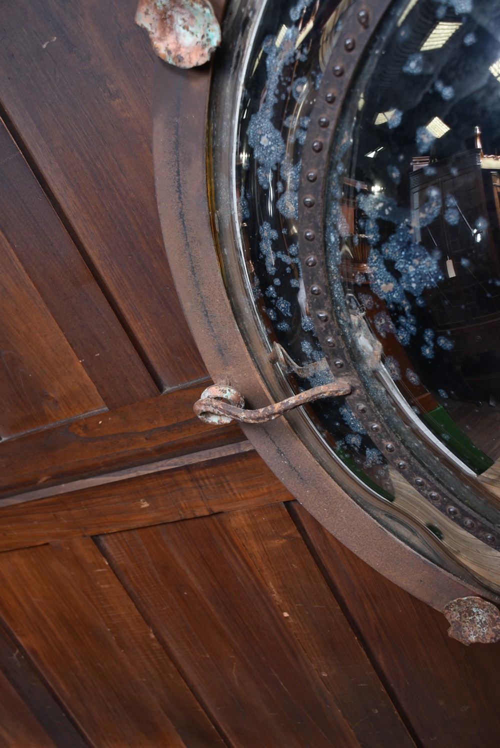 A circular convex wall mirror featuring a patinated dark metal frame, riveted inner rim, forged scroll mounts, and foxed glass reflection. View XI