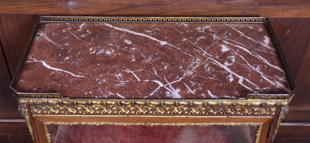 A French Louis XV style timber vitrine featuring a red marble top, gilded mounts, a glass front door, and a red velvet interior. View VI