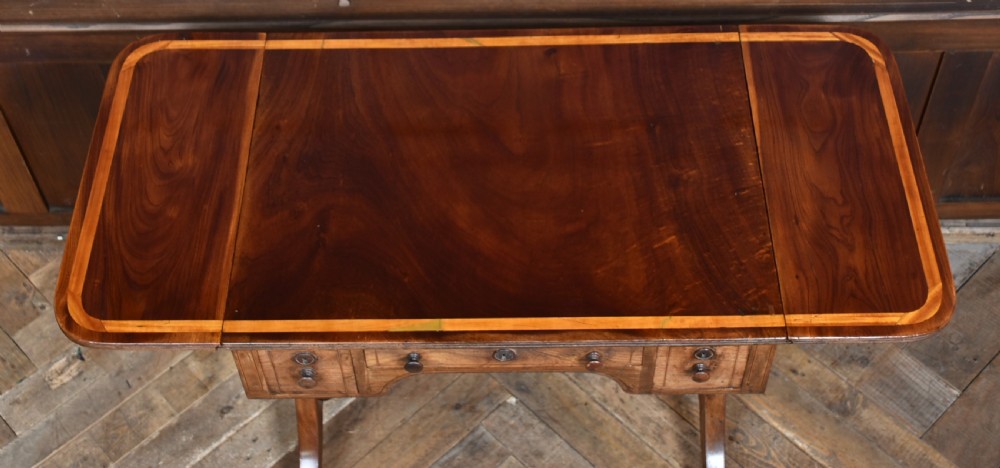 A Regency rosewood sofa table featuring a crossbanded drop-leaf top, shallow drawers with wooden knobs, curved trestle legs, and brass castors. View III