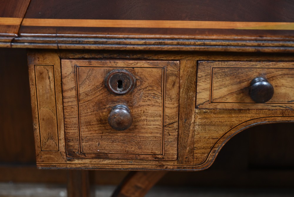A Regency rosewood sofa table featuring a crossbanded drop-leaf top, shallow drawers with wooden knobs, curved trestle legs, and brass castors. View V