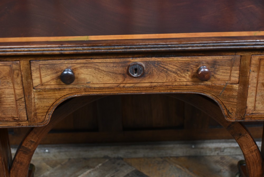 A Regency rosewood sofa table featuring a crossbanded drop-leaf top, shallow drawers with wooden knobs, curved trestle legs, and brass castors. View VII