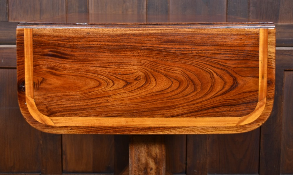 A Regency rosewood sofa table featuring a crossbanded drop-leaf top, shallow drawers with wooden knobs, curved trestle legs, and brass castors. View XIV