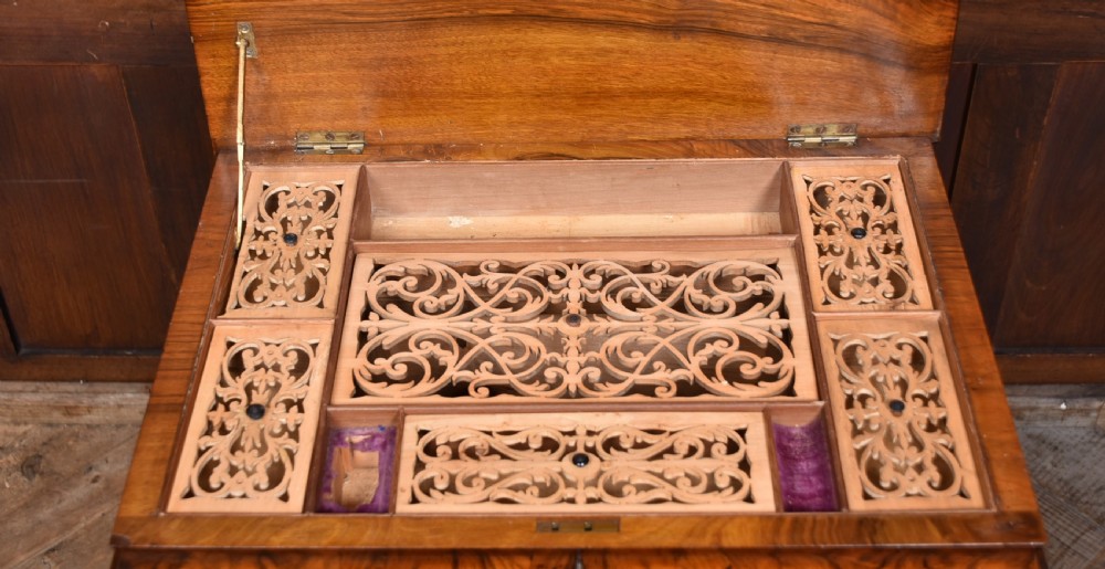 A Victorian burr walnut sewing table featuring a rectangular top above a tapered storage well, supported by turned carved columns, a central stretcher, and scroll feet on brass castors. View X