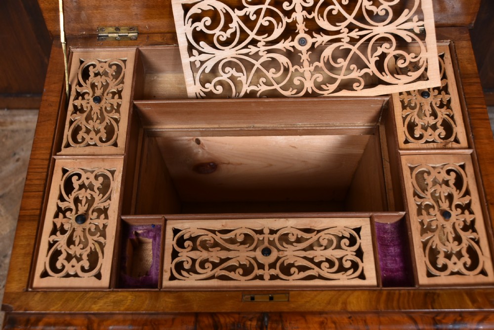 A Victorian burr walnut sewing table featuring a rectangular top above a tapered storage well, supported by turned carved columns, a central stretcher, and scroll feet on brass castors. View XI