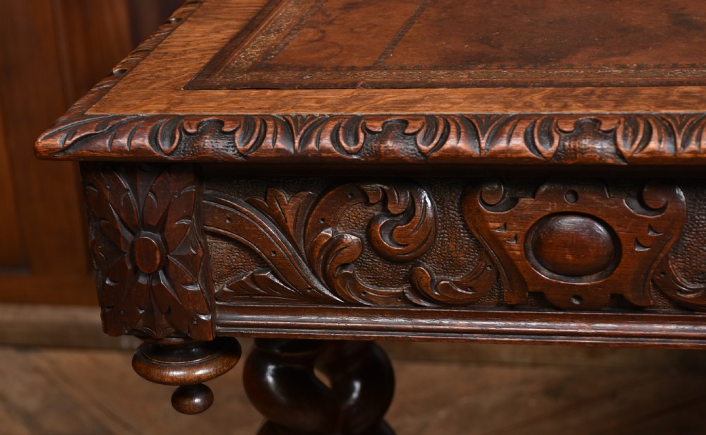 A Victorian carved dark oak writing table featuring a central Green Man mask, inset leather writing surface, and barley twist stretchers. View VI