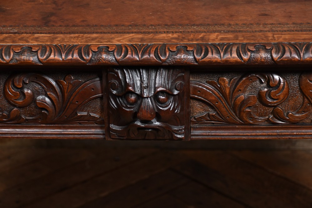 A Victorian carved dark oak writing table featuring a central Green Man mask, inset leather writing surface, and barley twist stretchers. View VII