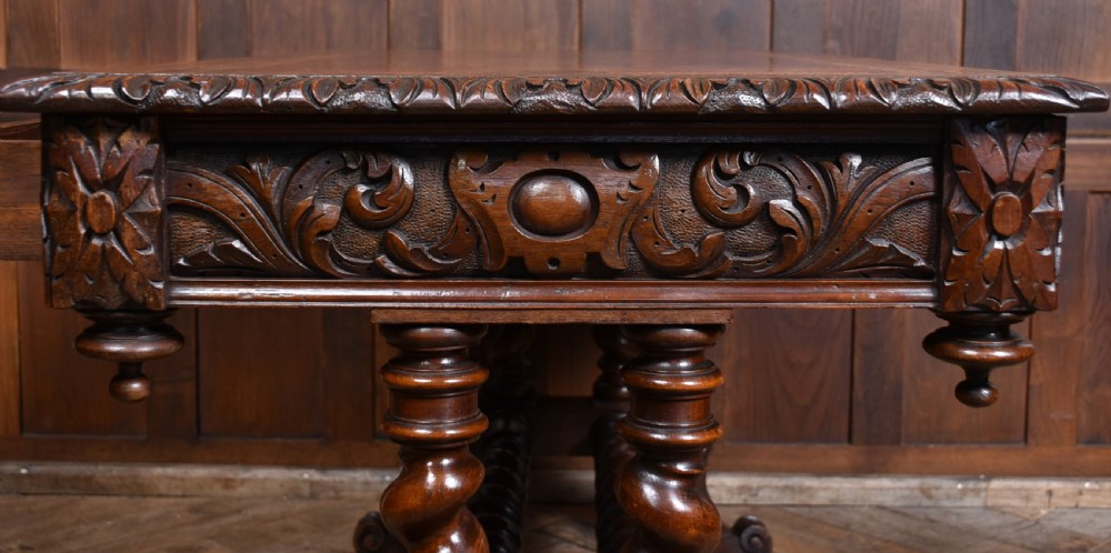 A Victorian carved dark oak writing table featuring a central Green Man mask, inset leather writing surface, and barley twist stretchers. View XVI