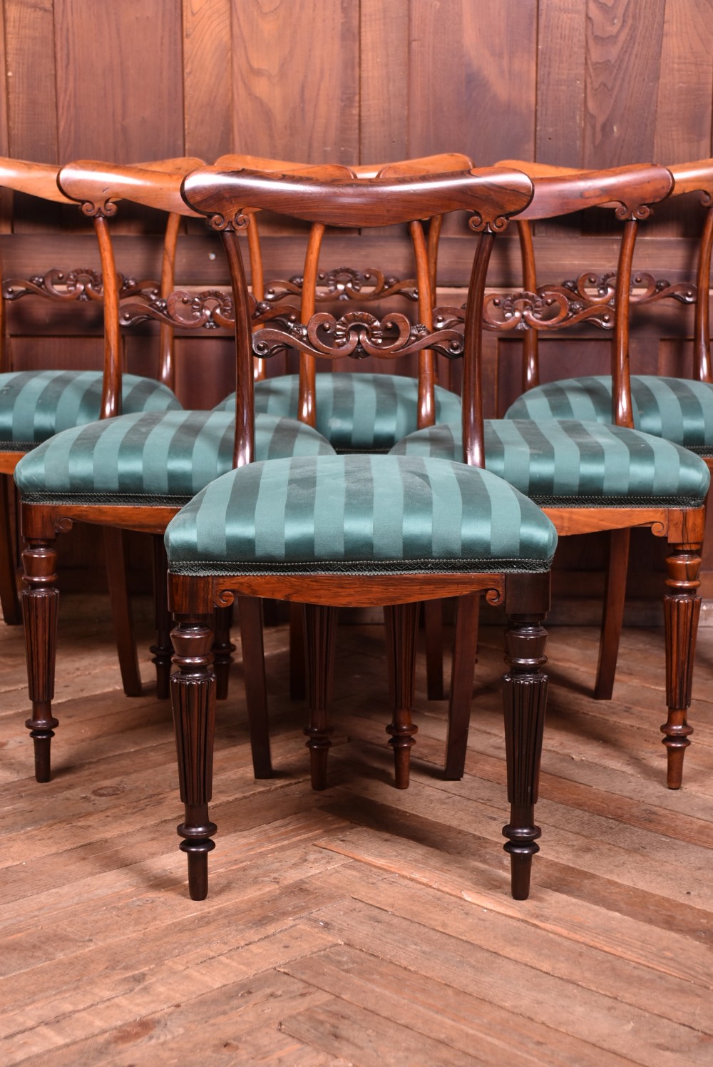 A set of six Victorian rosewood dining chairs featuring carved crest rails, decorative mid-rails, fluted turned front legs, and green striped upholstered seats. View II