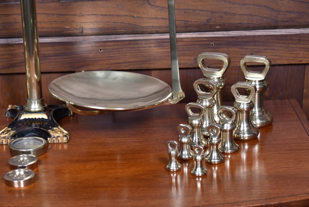 An Edwardian brass shopkeeper balance scale set on a central column base with two suspended pans and matching brass weights. View II