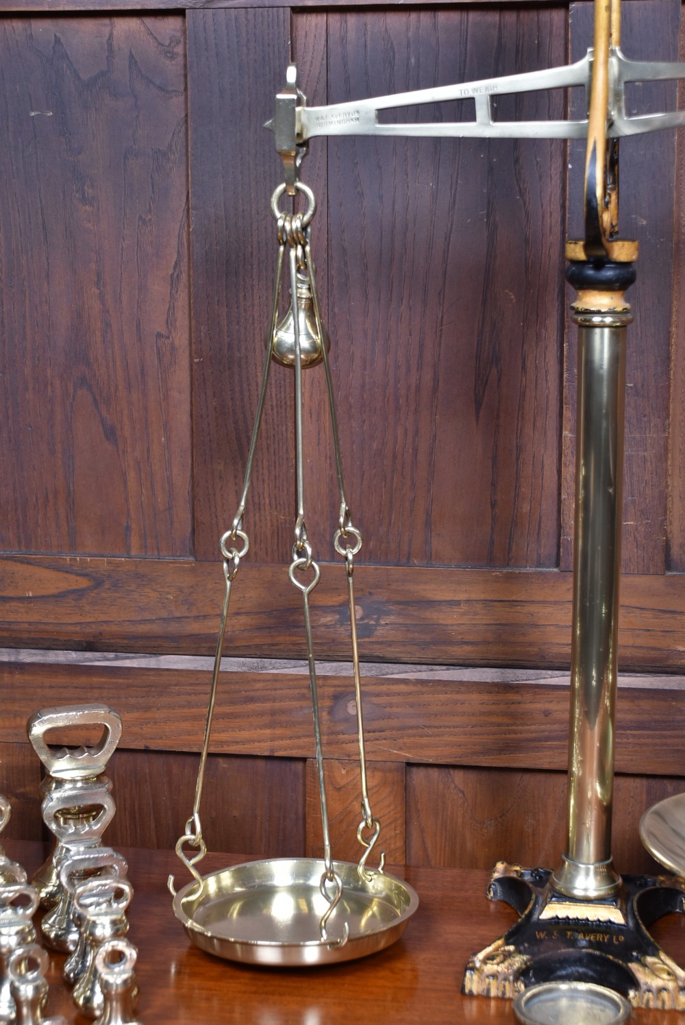 An Edwardian brass shopkeeper balance scale set on a central column base with two suspended pans and matching brass weights. View V