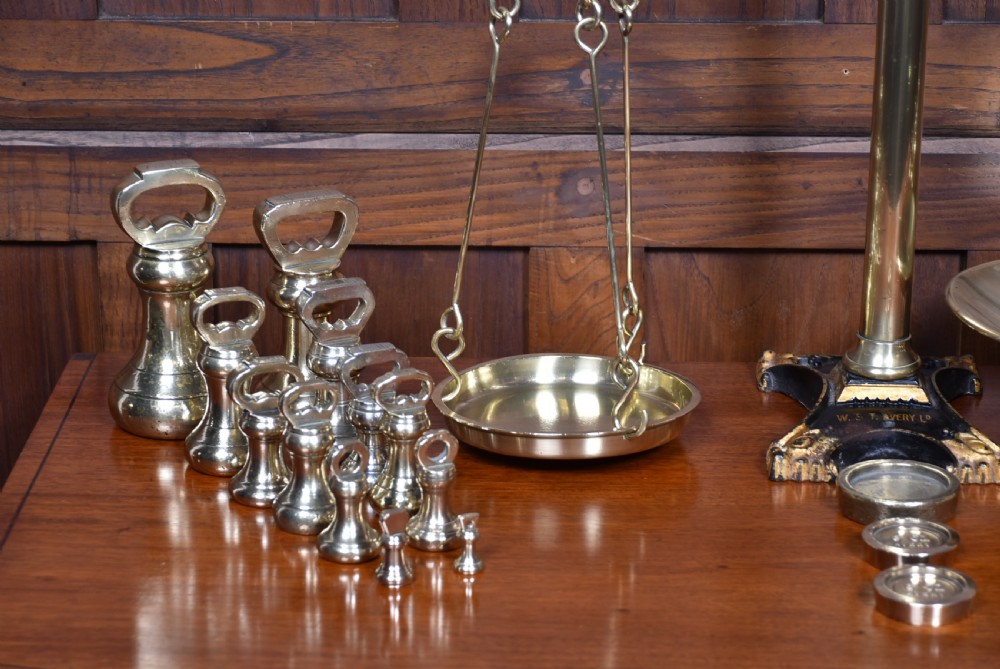 An Edwardian brass shopkeeper balance scale set on a central column base with two suspended pans and matching brass weights. View VI