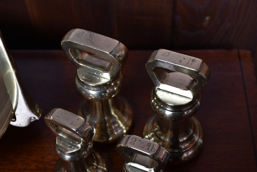 An Edwardian brass shopkeeper balance scale set on a central column base with two suspended pans and matching brass weights. View XII