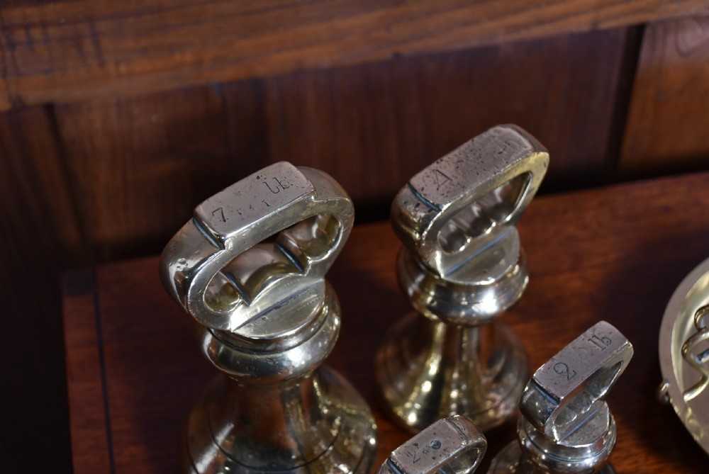 An Edwardian brass shopkeeper balance scale set on a central column base with two suspended pans and matching brass weights. View XIII