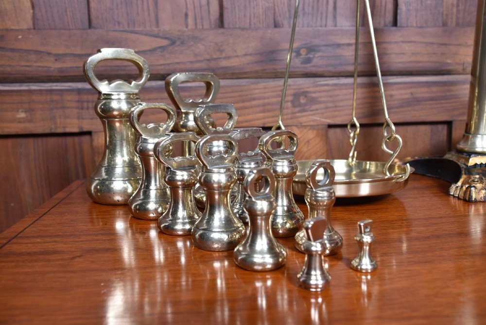 An Edwardian brass shopkeeper balance scale set on a central column base with two suspended pans and matching brass weights. View XV