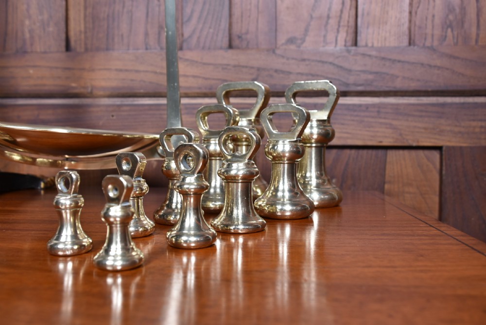 An Edwardian brass shopkeeper balance scale set on a central column base with two suspended pans and matching brass weights. View XVI