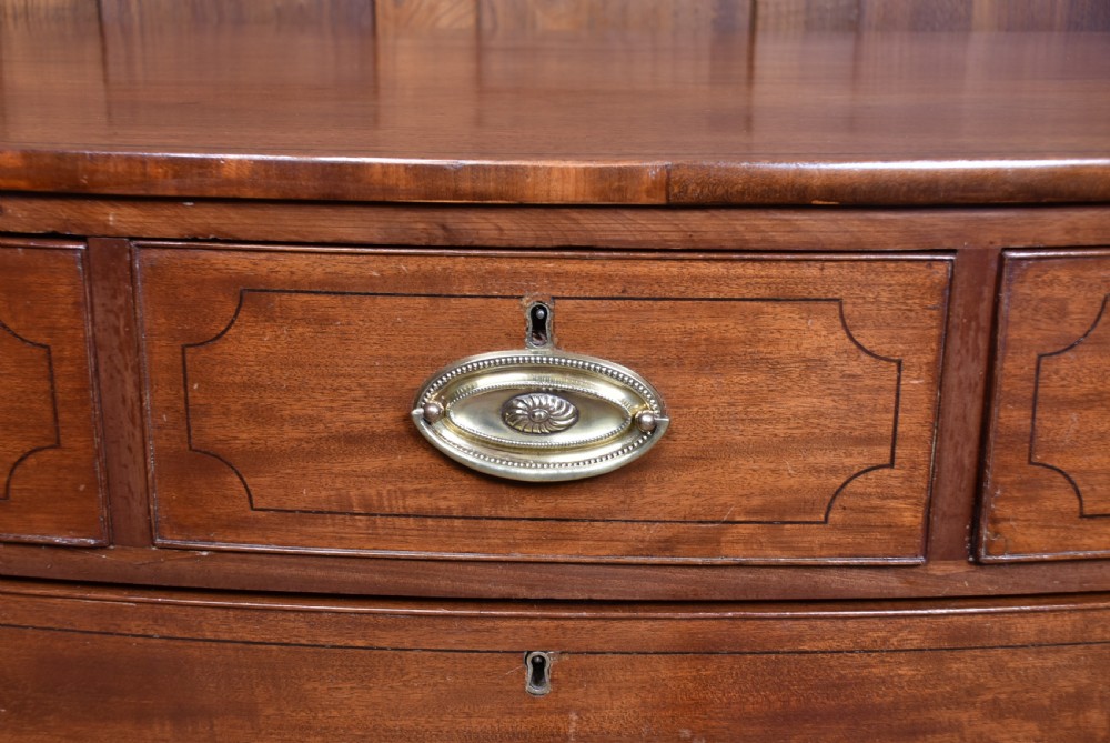 A Georgian mahogany bowfront chest of drawers featuring brass oval plate handles, three small upper drawers, three long lower drawers, and splayed bracket feet. View III