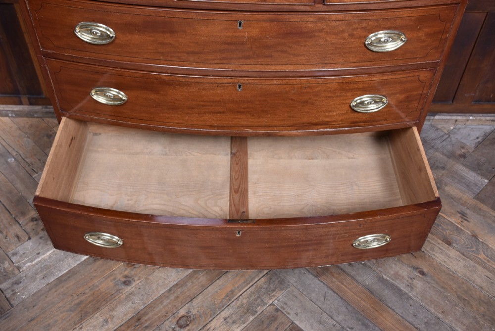 A Georgian mahogany bowfront chest of drawers featuring brass oval plate handles, three small upper drawers, three long lower drawers, and splayed bracket feet. View VI