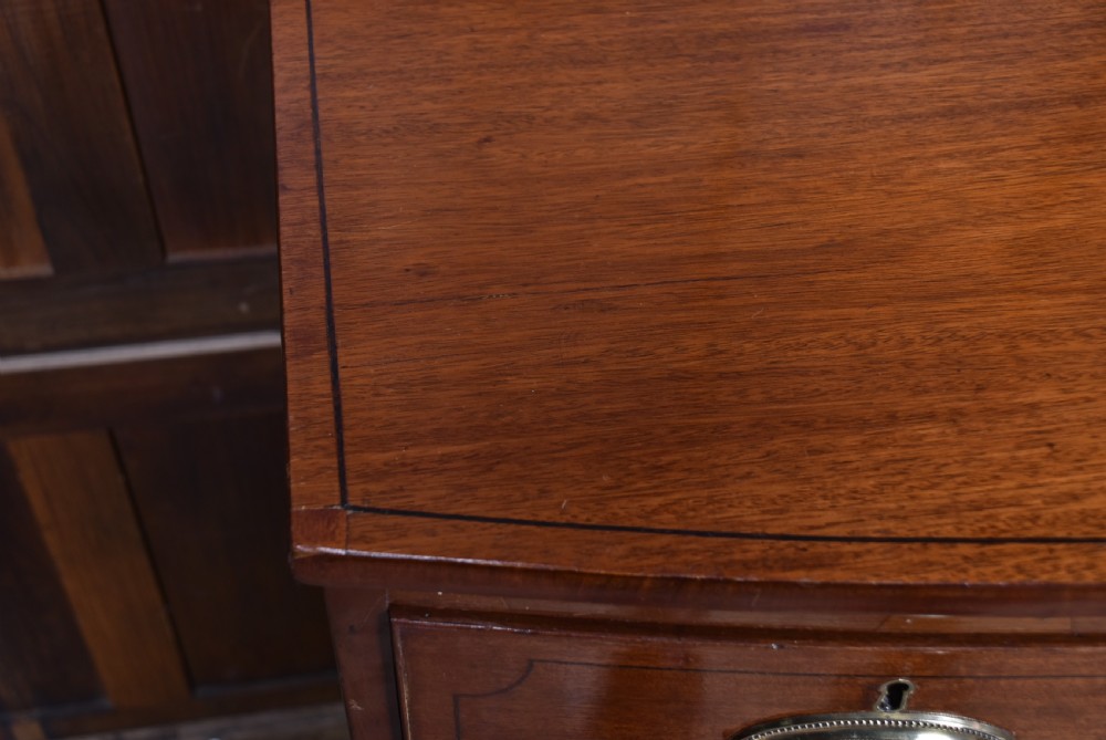 A Georgian mahogany bowfront chest of drawers featuring brass oval plate handles, three small upper drawers, three long lower drawers, and splayed bracket feet. View VIII