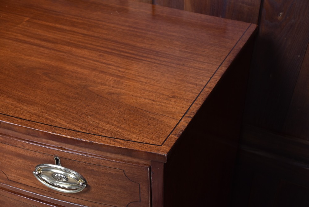 A Georgian mahogany bowfront chest of drawers featuring brass oval plate handles, three small upper drawers, three long lower drawers, and splayed bracket feet. View X