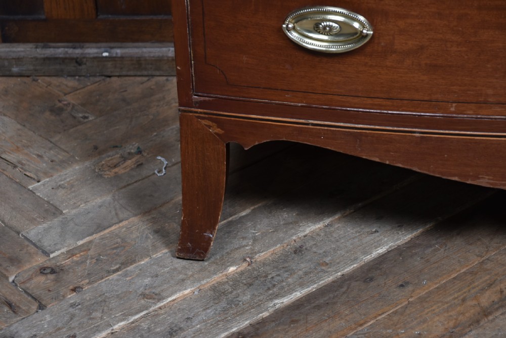 A Georgian mahogany bowfront chest of drawers featuring brass oval plate handles, three small upper drawers, three long lower drawers, and splayed bracket feet. View XII