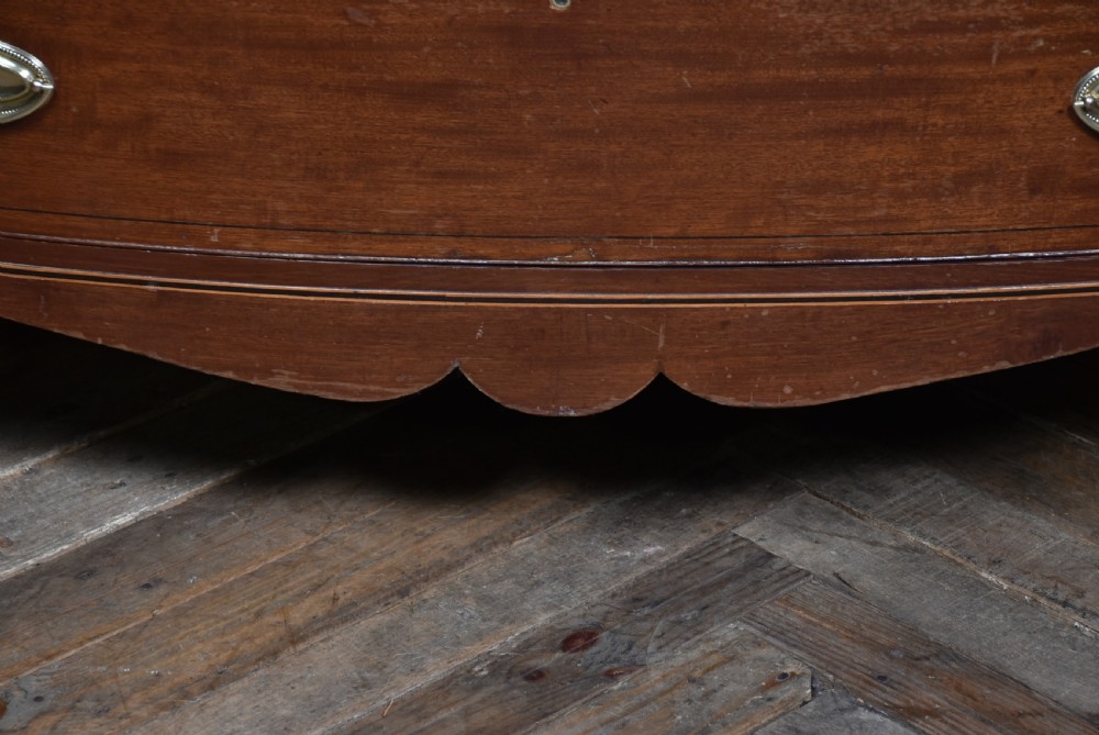 A Georgian mahogany bowfront chest of drawers featuring brass oval plate handles, three small upper drawers, three long lower drawers, and splayed bracket feet. View XIII