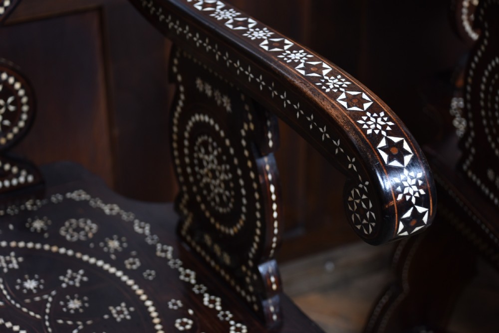 A pair of dark wood armchairs intricately decorated with white geometric bone inlay throughout the backrests, seats, arms, and legs. View IX