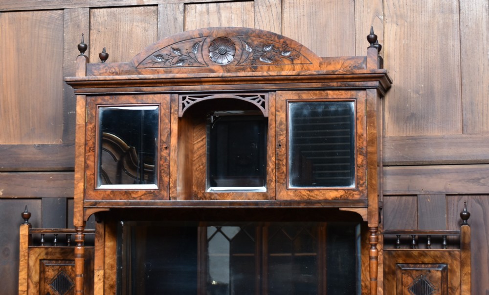 A late Victorian burr walnut display cabinet featuring tiered shelving, multiple mirror panels, turned support pillars, and carved lower cabinet doors. View II
