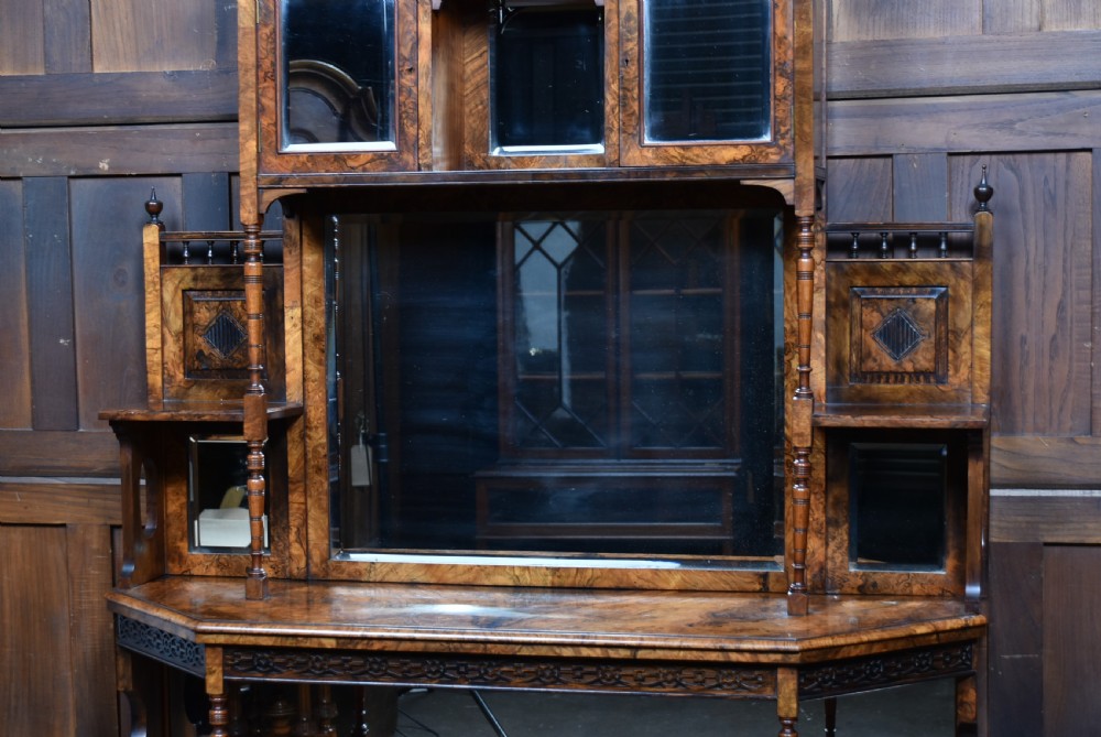 A late Victorian burr walnut display cabinet featuring tiered shelving, multiple mirror panels, turned support pillars, and carved lower cabinet doors. View V