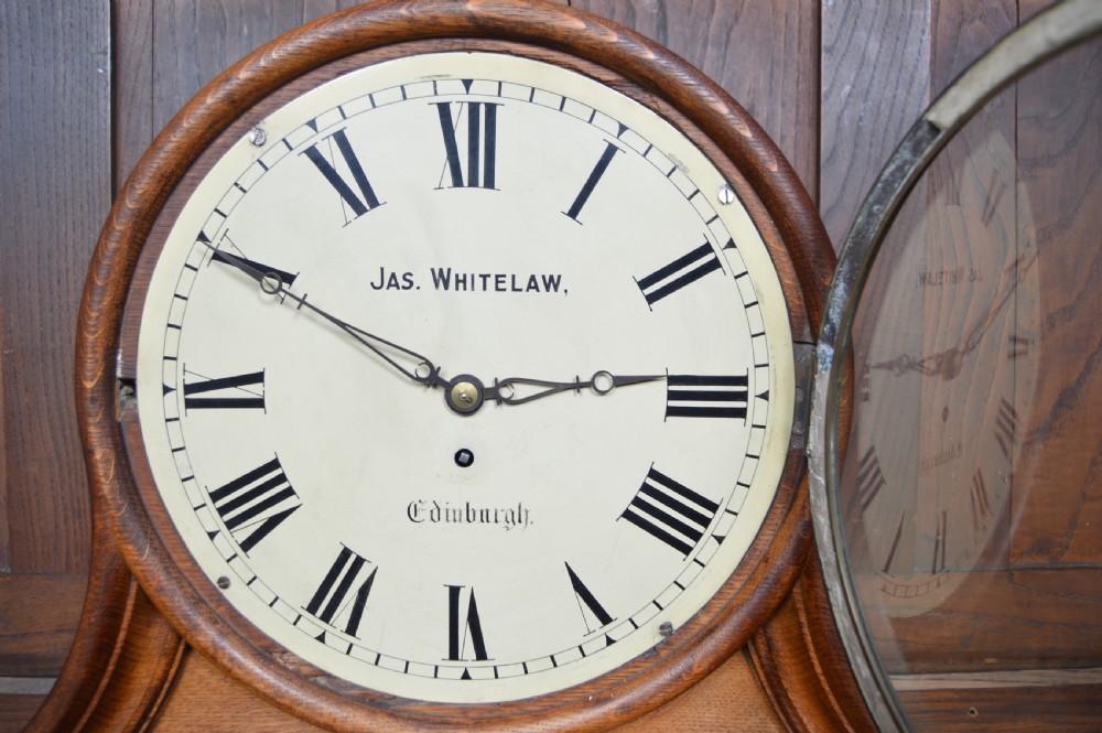 An Edwardian oak mantel clock featuring a curved wooden frame, a brass-rimmed glass face with Roman numerals, and the inscription Jas Whitelaw Edinburgh. View VI
