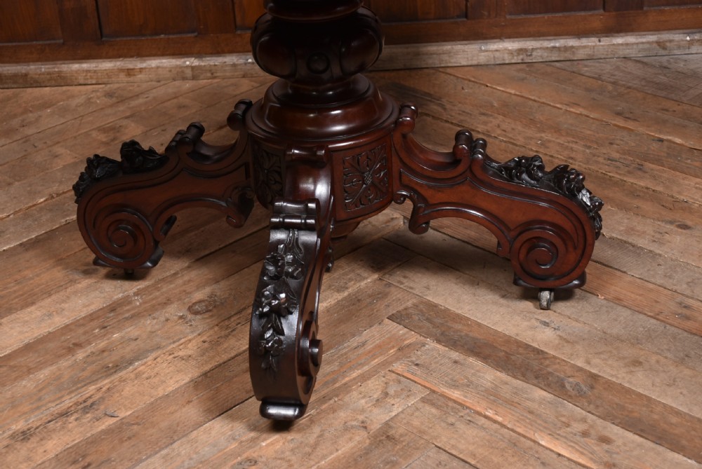 A Victorian walnut centre table featuring a violin-shaped contoured top, a central carved bulbous pedestal column, and four scrolled cabriole legs on brass castors. View II