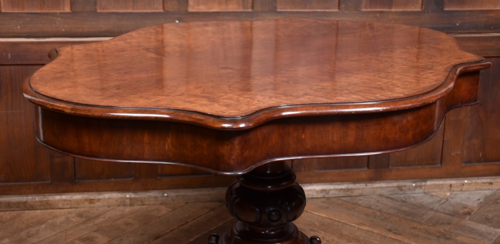 A Victorian walnut centre table featuring a violin-shaped contoured top, a central carved bulbous pedestal column, and four scrolled cabriole legs on brass castors. View V