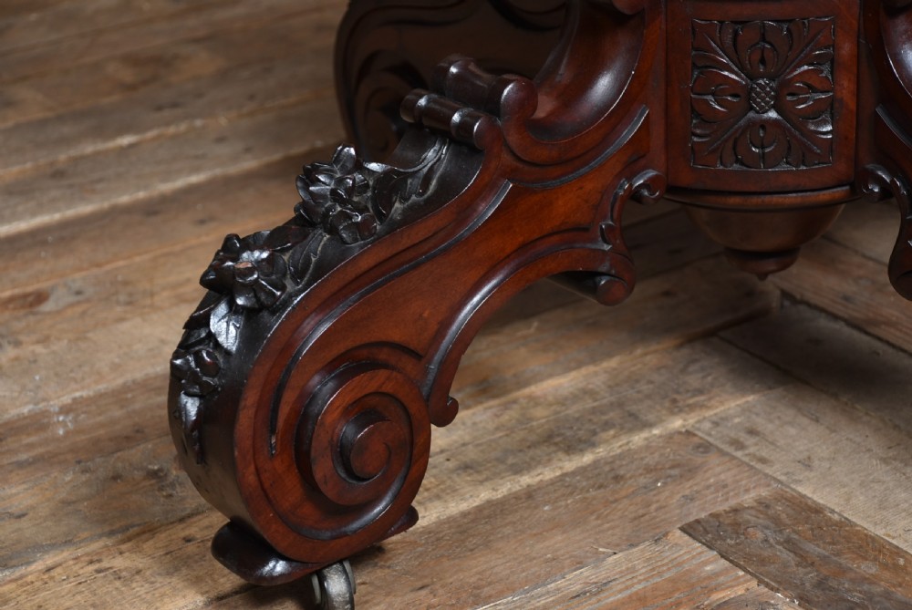 A Victorian walnut centre table featuring a violin-shaped contoured top, a central carved bulbous pedestal column, and four scrolled cabriole legs on brass castors. View X