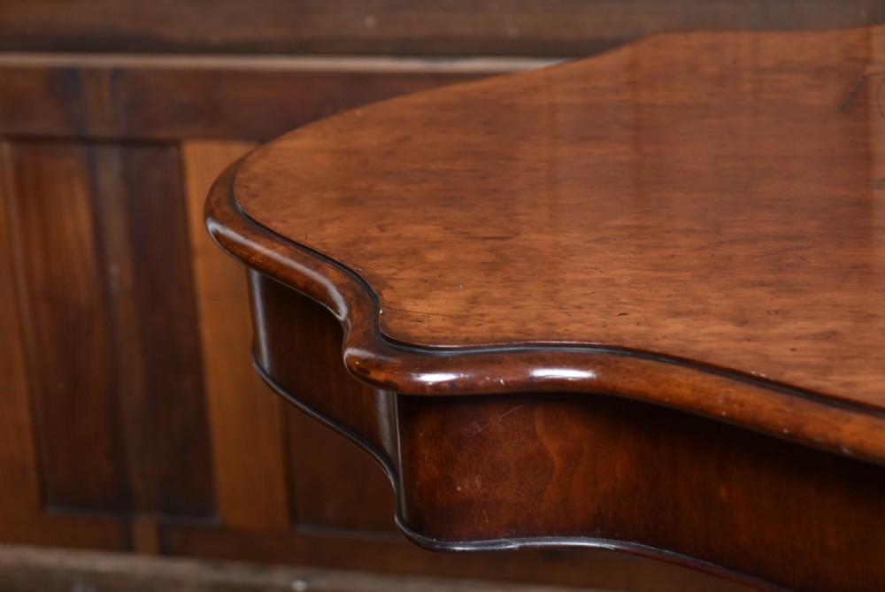 A Victorian walnut centre table featuring a violin-shaped contoured top, a central carved bulbous pedestal column, and four scrolled cabriole legs on brass castors. View XII