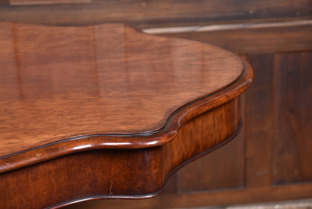 A Victorian walnut centre table featuring a violin-shaped contoured top, a central carved bulbous pedestal column, and four scrolled cabriole legs on brass castors. View XIII
