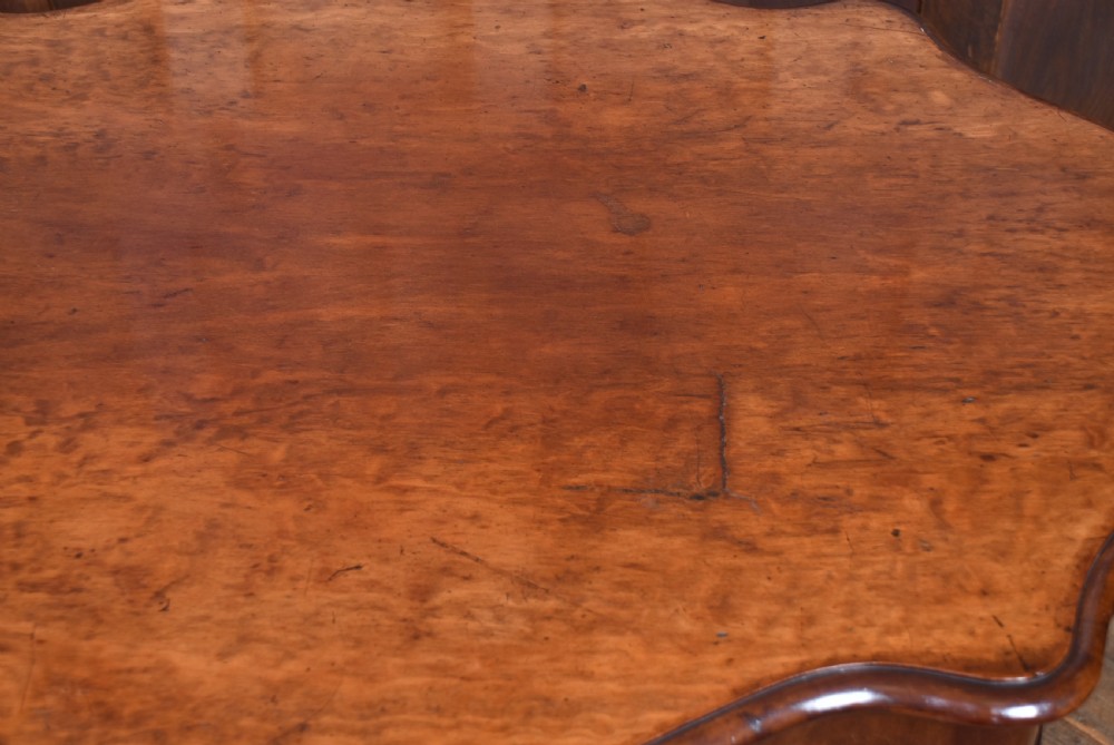 A Victorian walnut centre table featuring a violin-shaped contoured top, a central carved bulbous pedestal column, and four scrolled cabriole legs on brass castors. View XVI