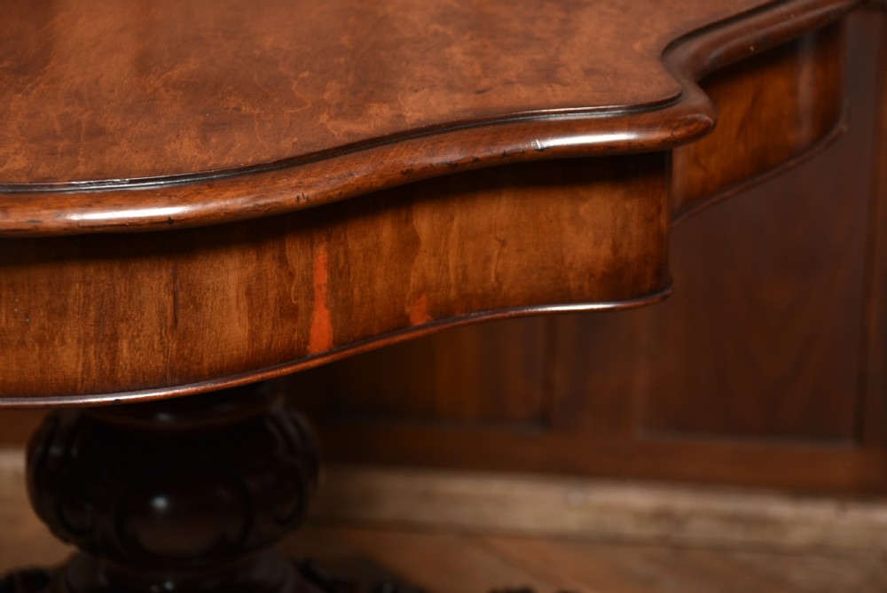 A Victorian walnut centre table featuring a violin-shaped contoured top, a central carved bulbous pedestal column, and four scrolled cabriole legs on brass castors. View XVIII