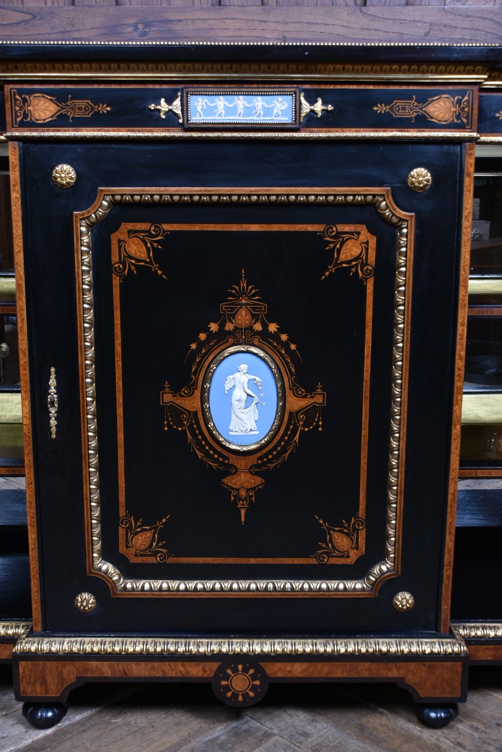 A Victorian ebonised and amboyna breakfront credenza featuring a central cupboard with a blue jasperware plaque flanked by open shelves and gilt fluted columns. View V
