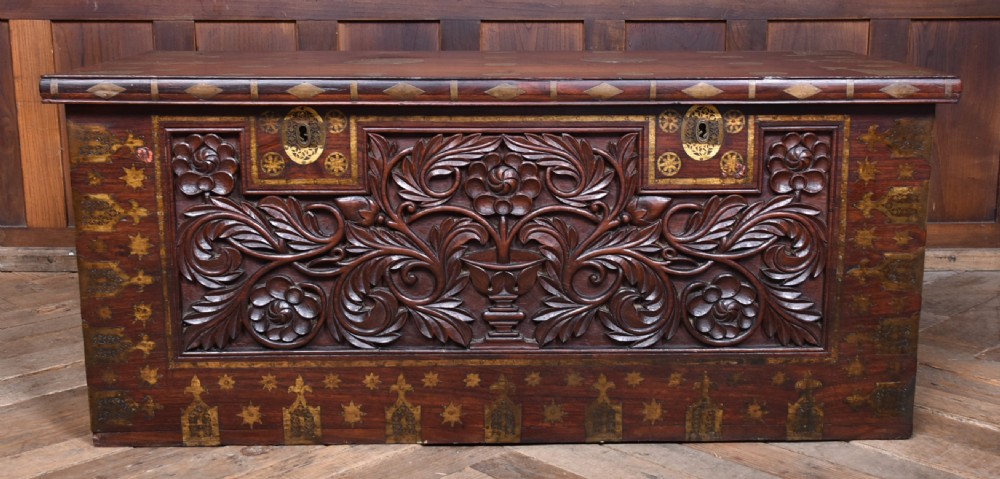 A dark reddish brown padouk wood storage chest featuring a relief-carved floral front panel and decorative brass metal mounts across the top lid and frame. View III