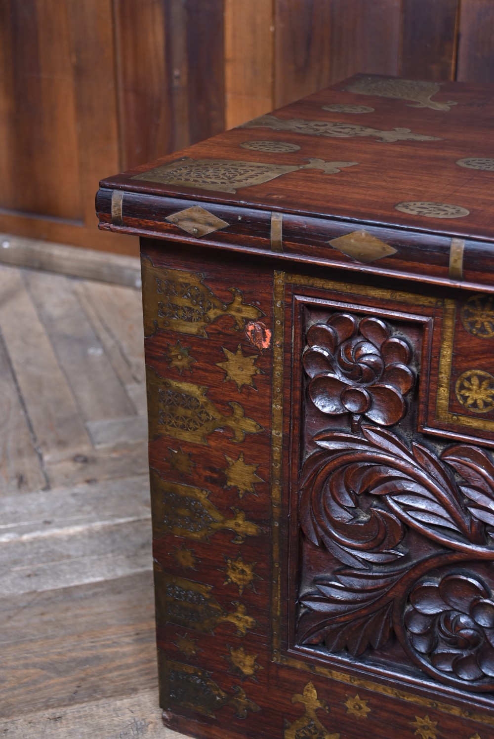 A dark reddish brown padouk wood storage chest featuring a relief-carved floral front panel and decorative brass metal mounts across the top lid and frame. View VIII