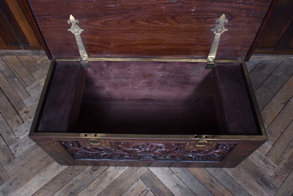 A dark reddish brown padouk wood storage chest featuring a relief-carved floral front panel and decorative brass metal mounts across the top lid and frame. View XI